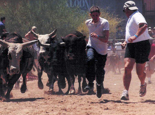 A man running with two bulls in the dirt.