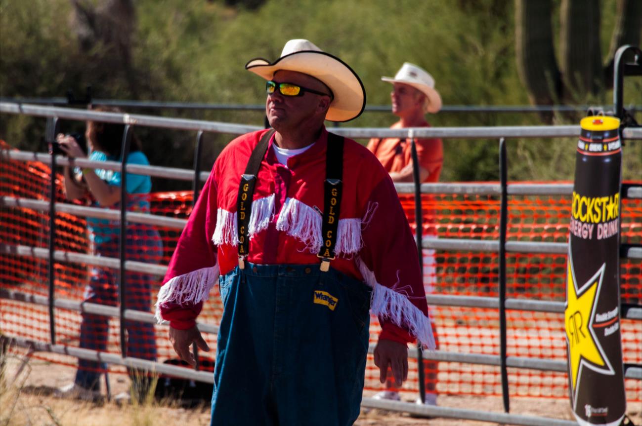 A man in cowboy attire standing next to a fence.