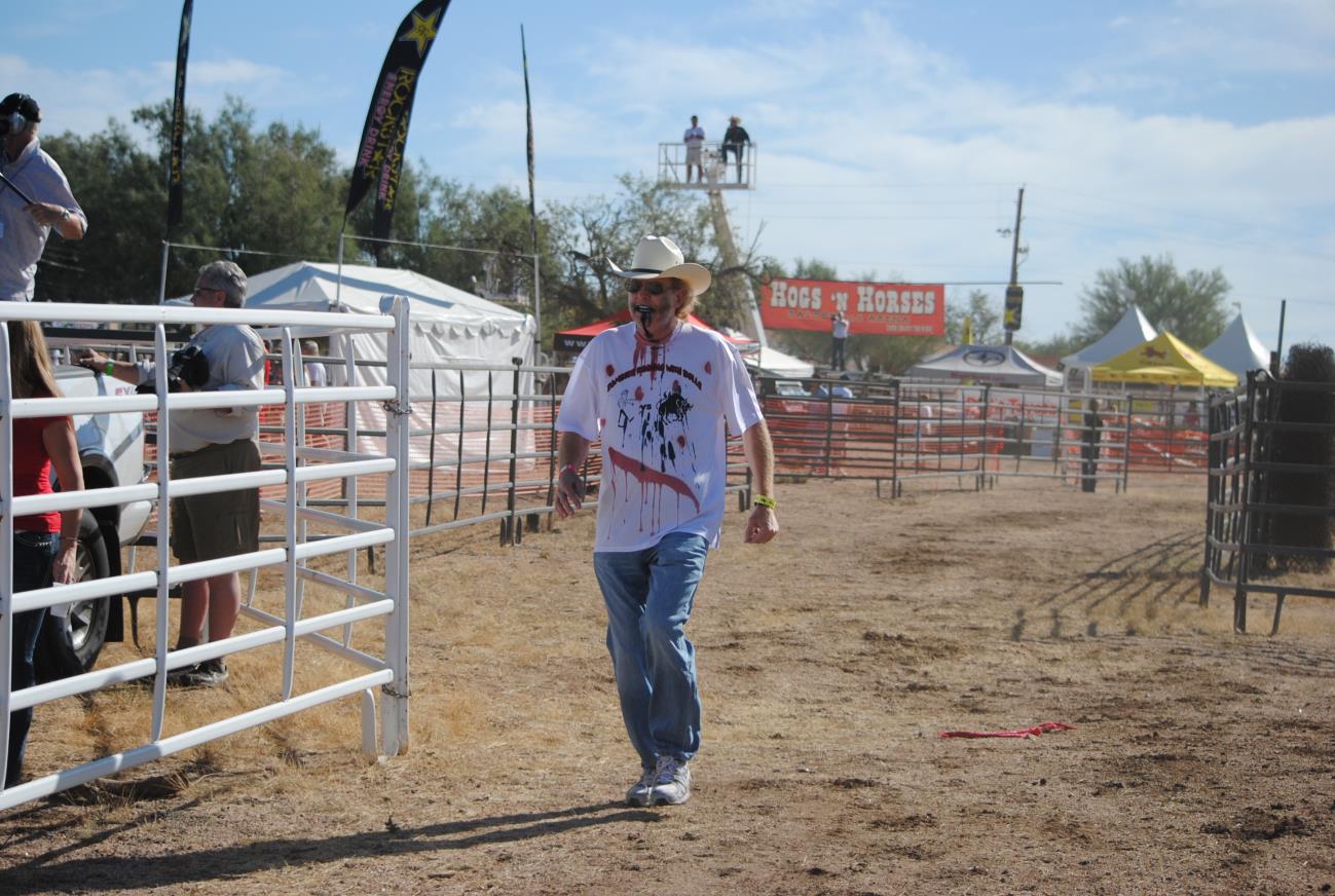 A man in cowboy hat walking across dirt field.